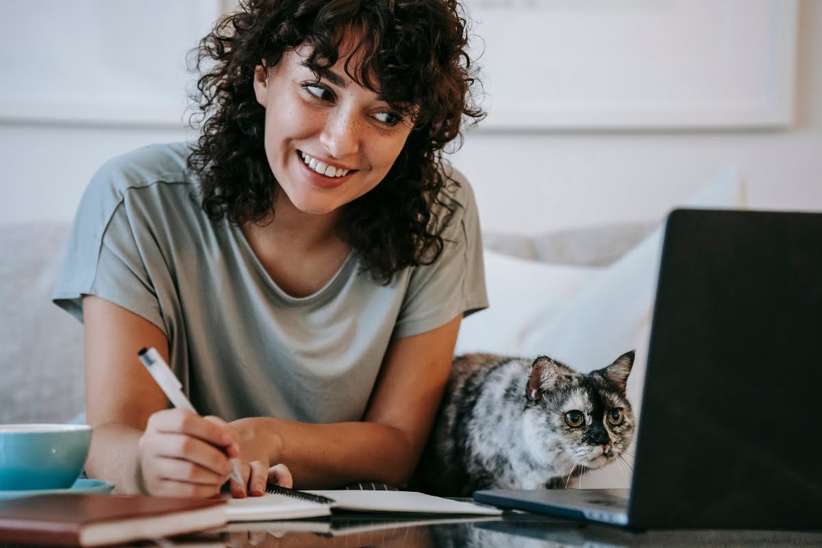 A woman writing copy on her laptop with a cat in front of her.