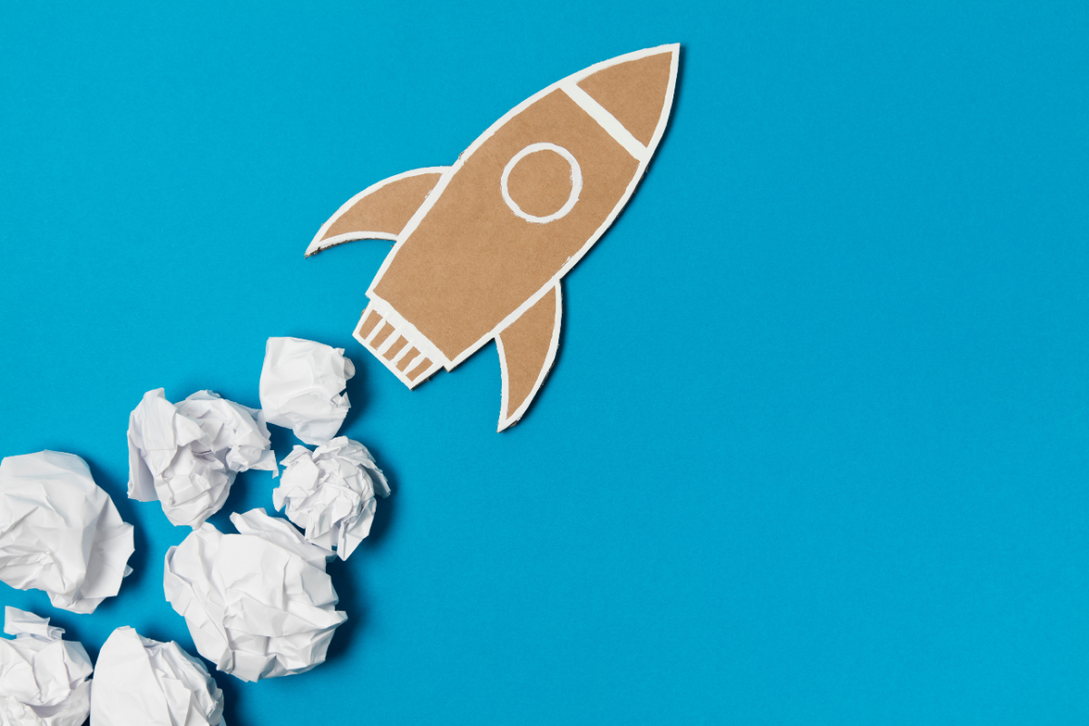 A paper rocket soaring through crumpled paper on a vibrant blue background.