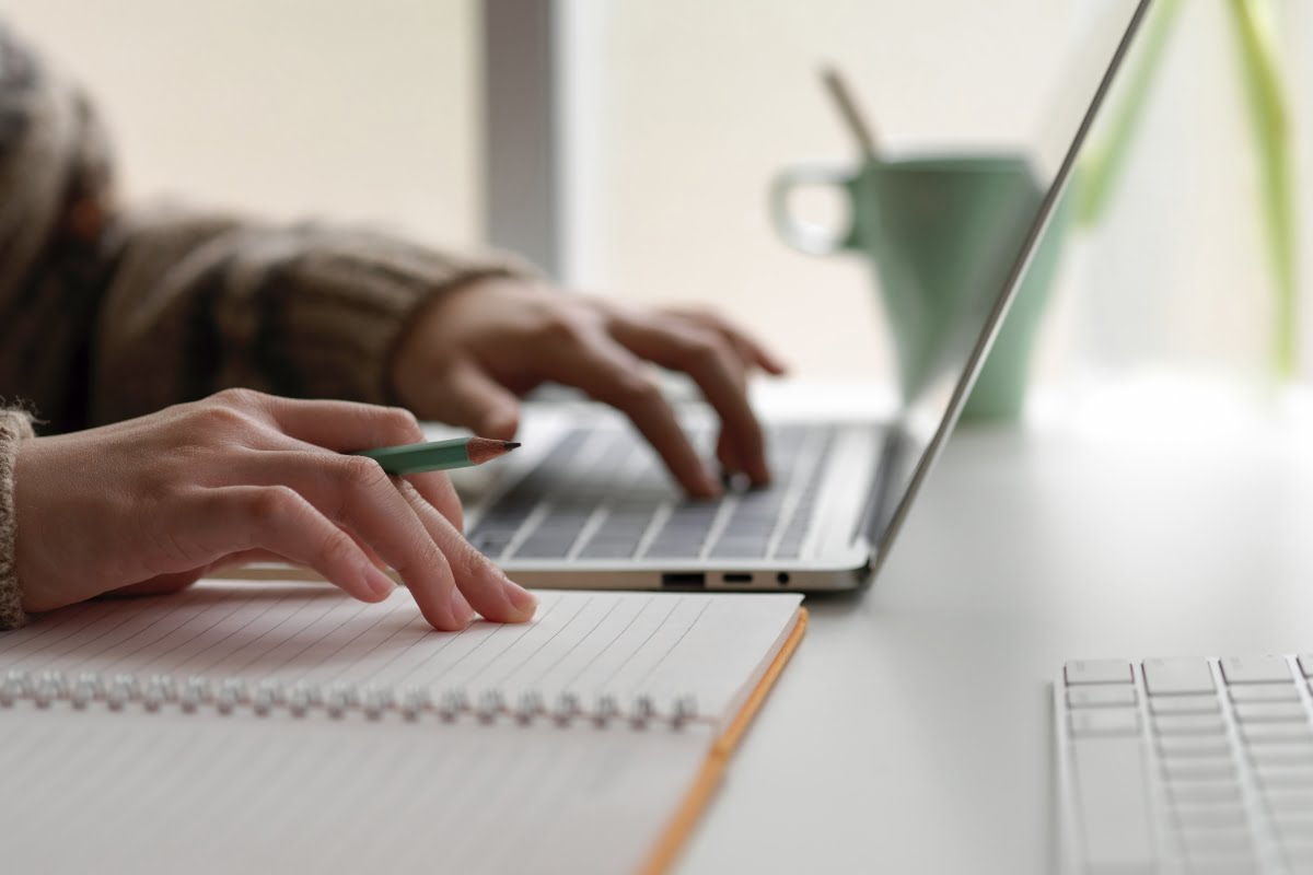 A person typing on a laptop at a desk while browsing through carpet cleaning ads.