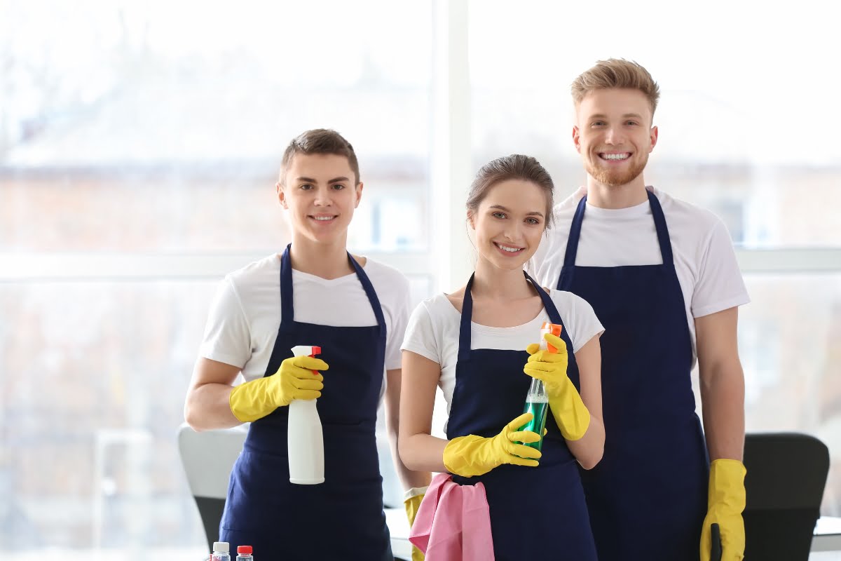 Three people in aprons showcasing cleaning supplies for advertising purposes.