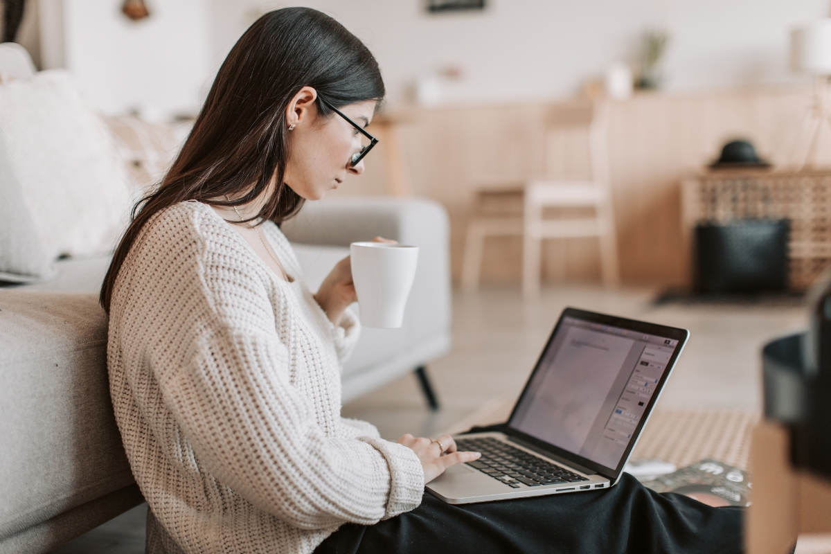 A woman, coffee in hand, sitting on the couch working on her laptop as she strategically plans her content marketing strategy.