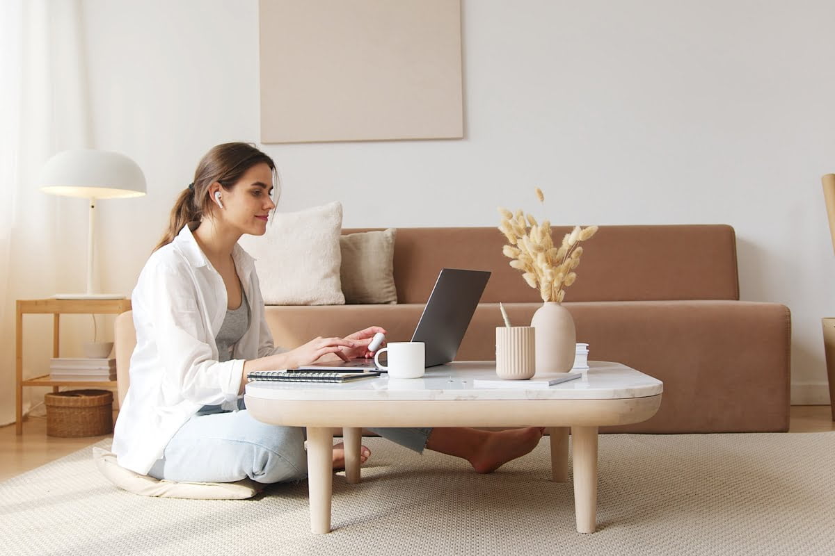 An evergreen content creator sitting on the floor with a laptop in her living room.