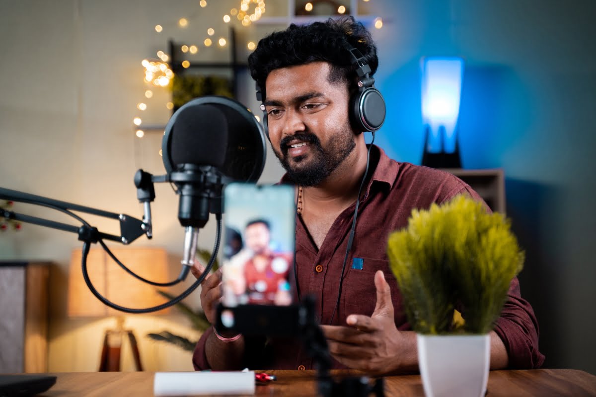 A man with headphones and a microphone sits in front of a table, producing evergreen content.