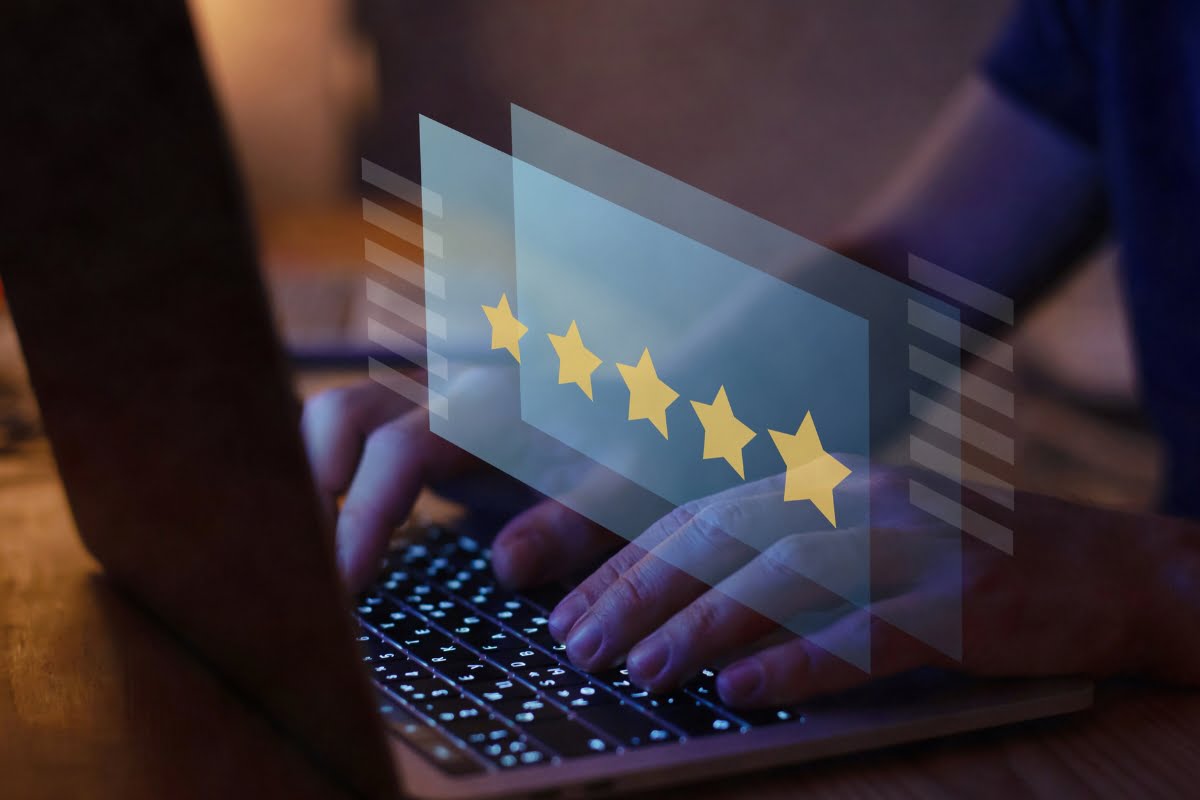 A person typing on a laptop with stars on it, trying to get more reviews on google.