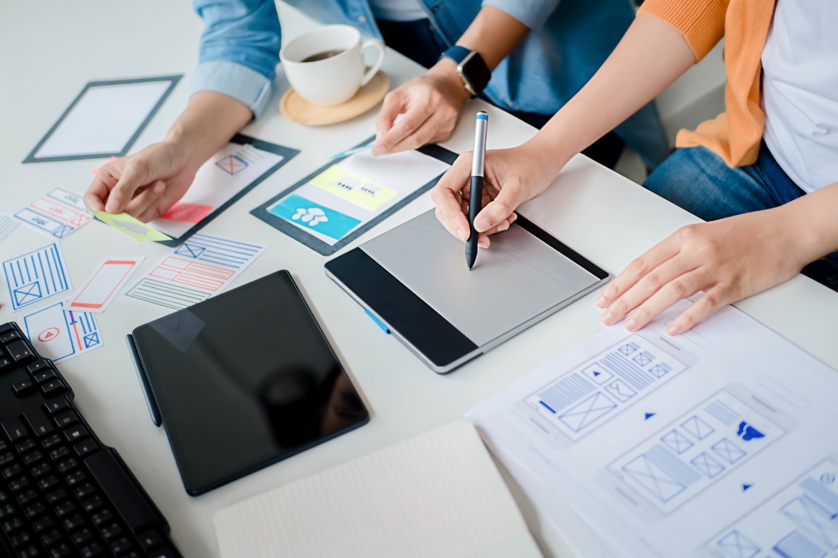 A group of people working at a desk with paper and pens.