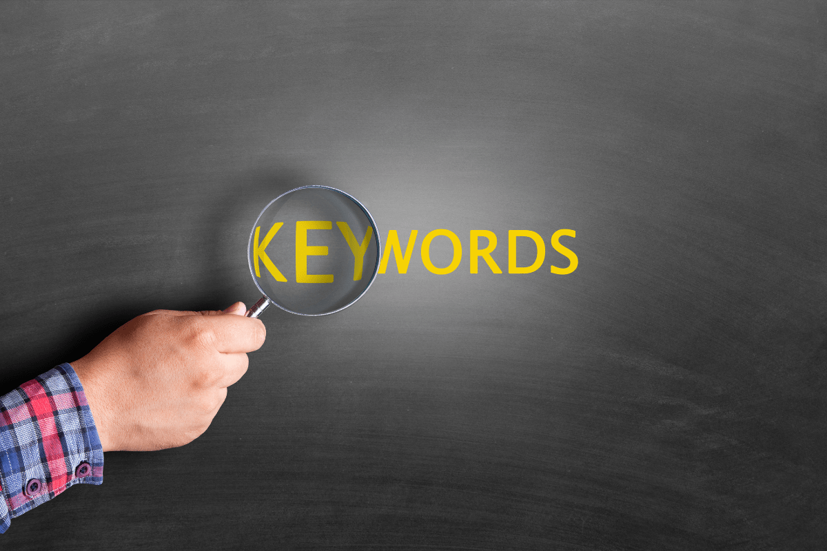 A hand holding a magnifying glass over the word "keywords."