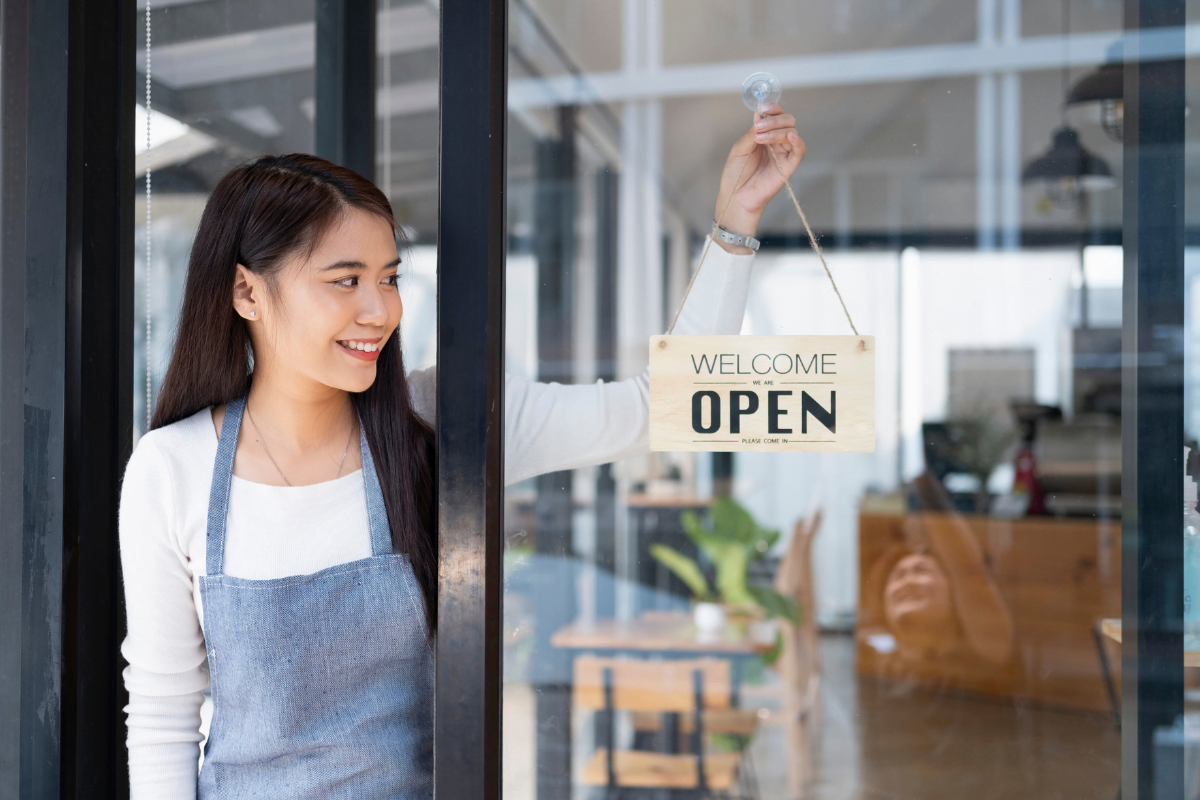 A woman is holding a welcome sign in front of a local shop.