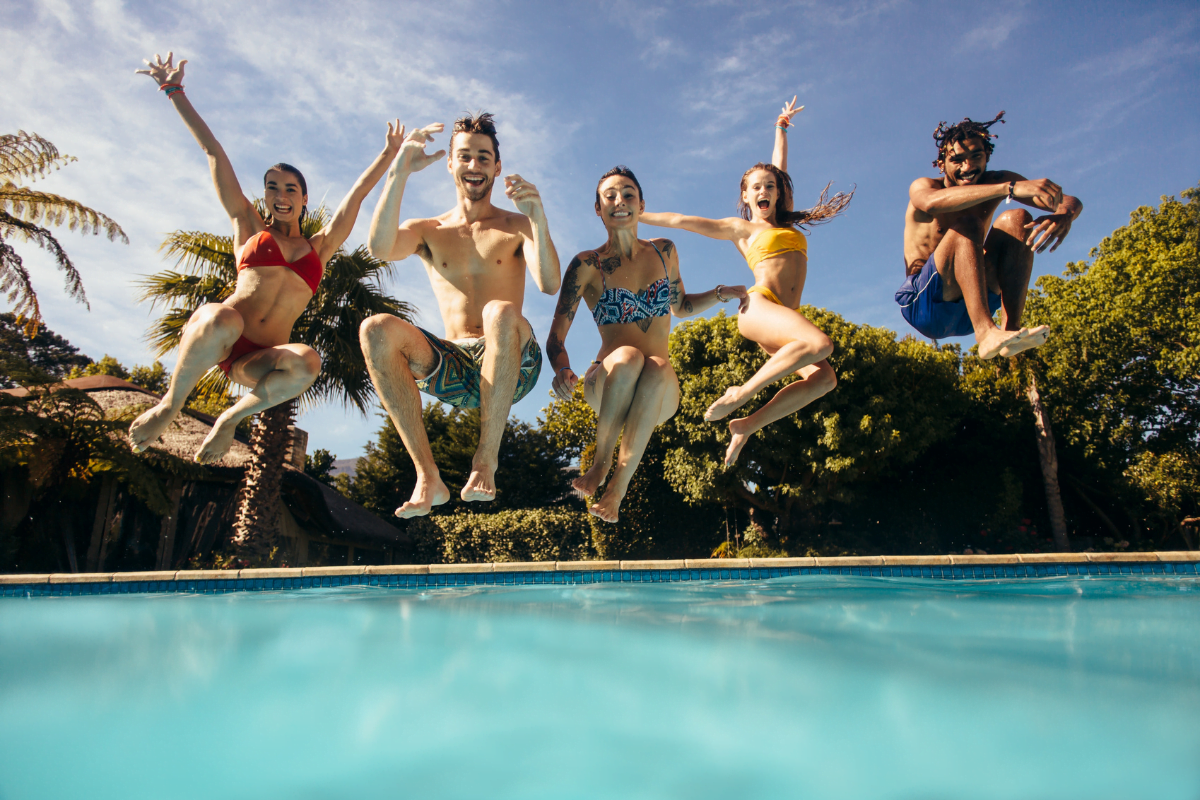 A group of people enthusiastically jumping into a refreshing swimming pool.