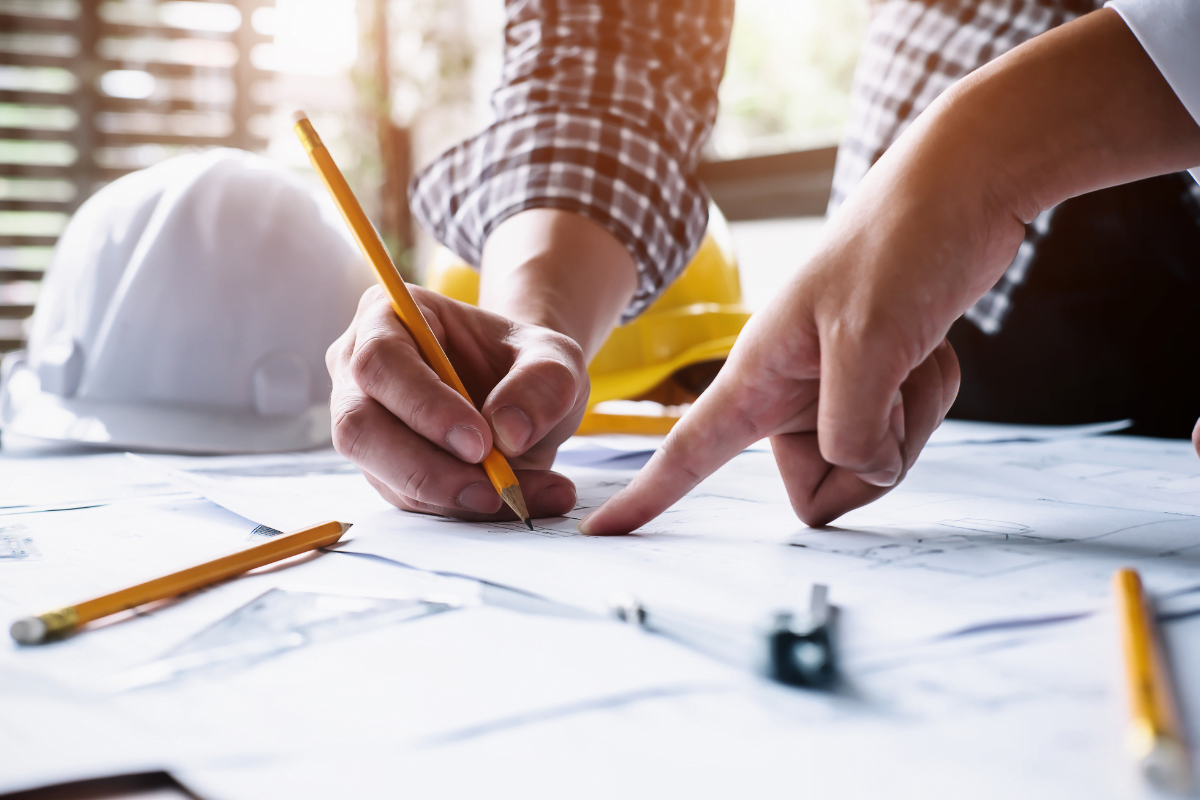 A person's hands holding a pencil and pointing at a drawing on a paper.