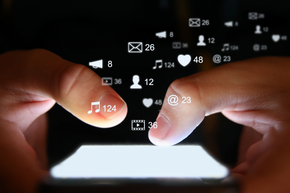 A person's hand is holding a cell phone with social media icons coming out of it, perfect for flooring companies looking to maximize their online presence.