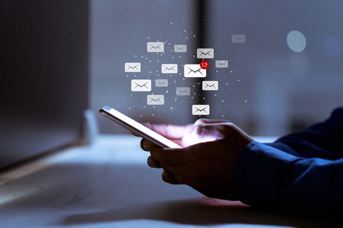 A person using a cell phone with email icons coming out of it while engaging in spa email marketing.