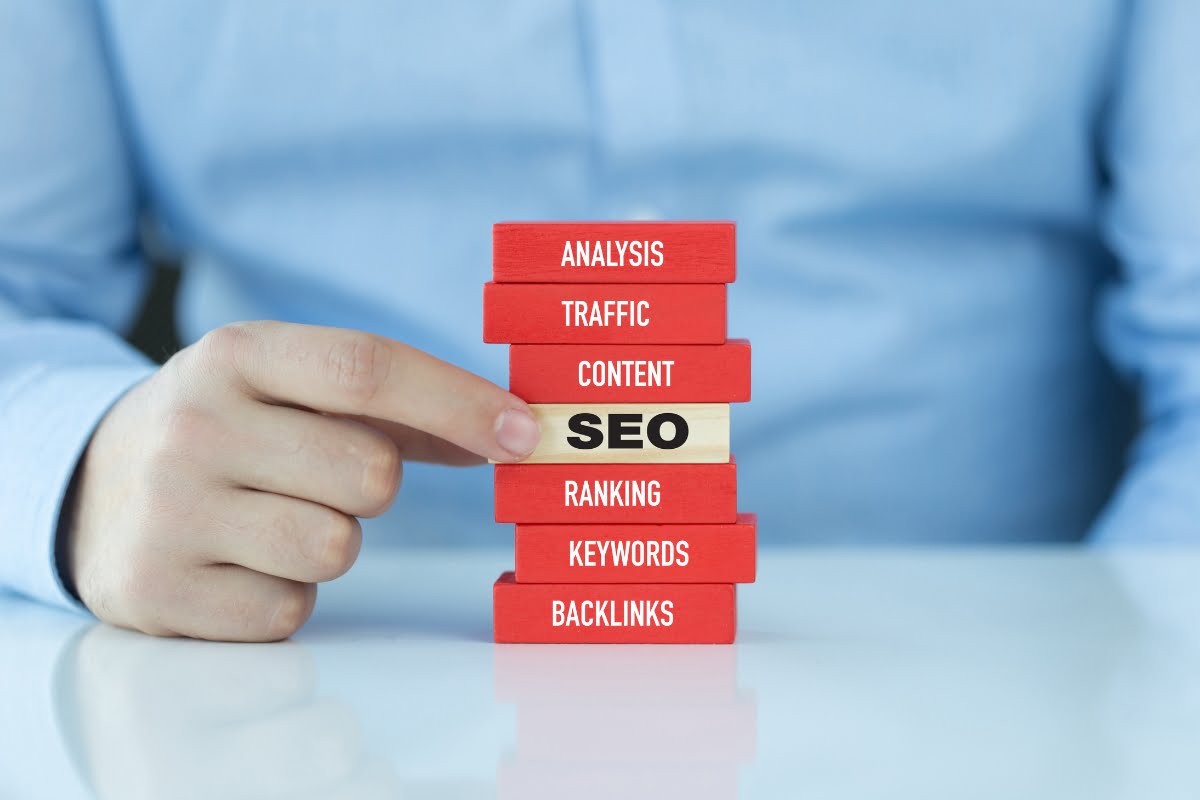 A man is pointing to a stack of red blocks with the word SEO, emphasizing its importance in the context of a website audit checklist.