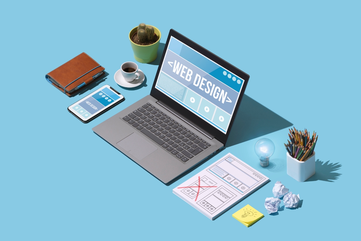 A laptop is sitting on a table next to a phone and other items, providing inspiration for simple website design ideas for beginners.