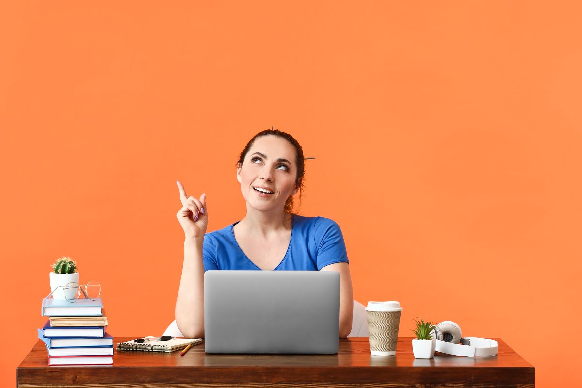 A woman sitting at a desk with a laptop, pointing to something on her updated website.