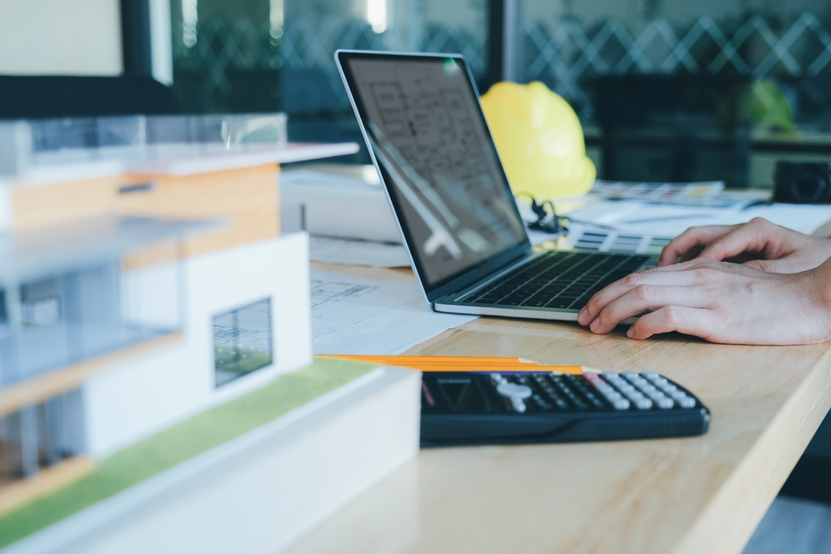 A person working on a laptop at a desk with a model of a house for contractor websites.