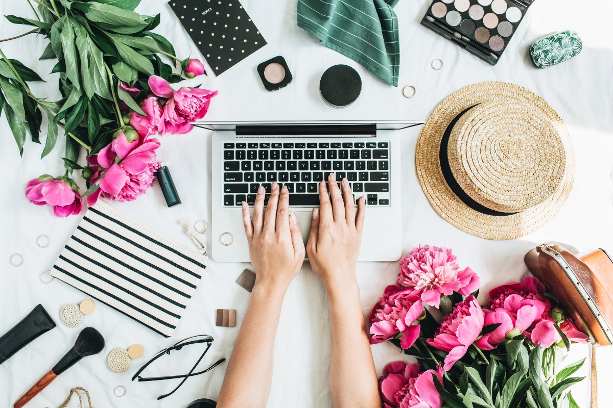 A woman's hands typing on a laptop with flowers nearby.