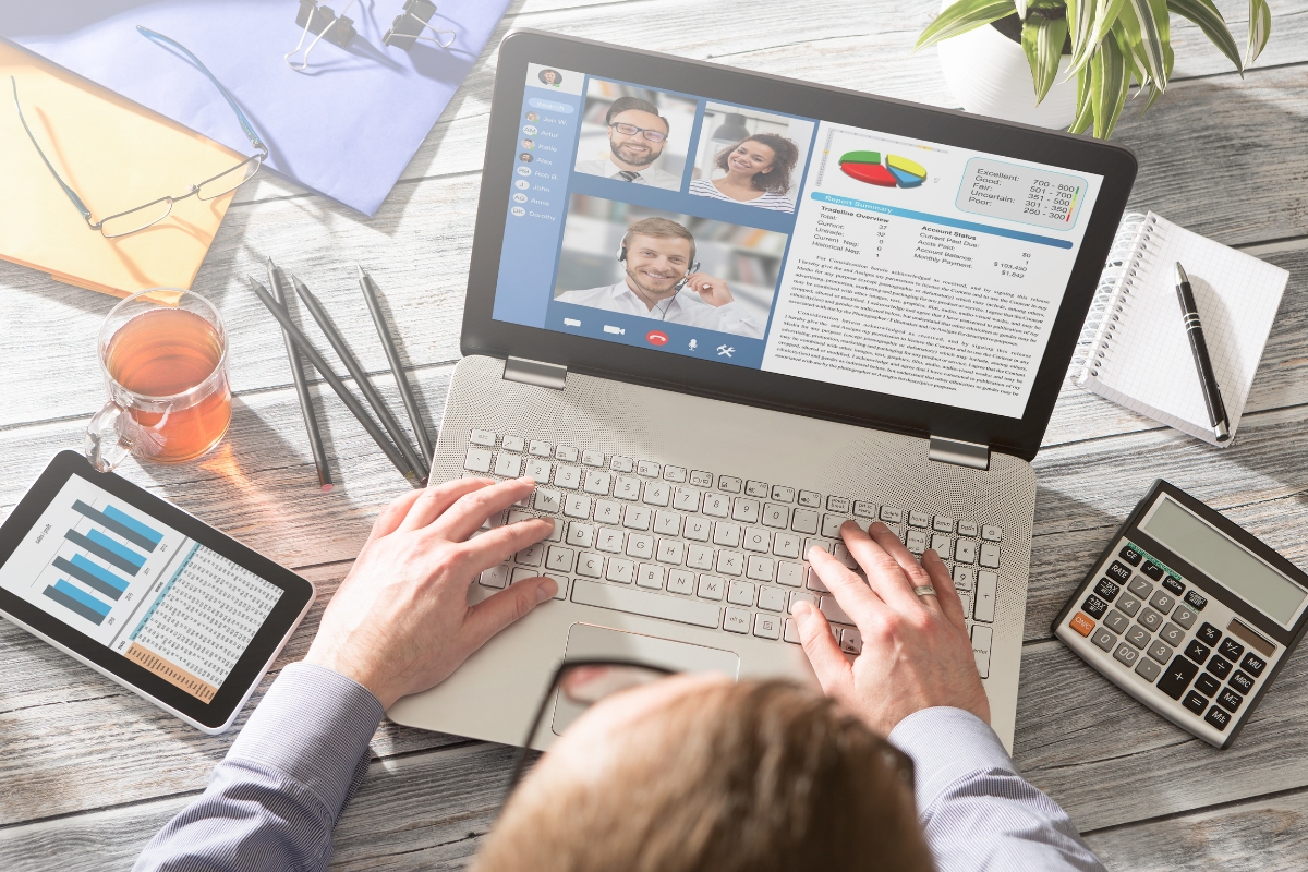 A man is guest posting on his laptop with a screen showing several people.