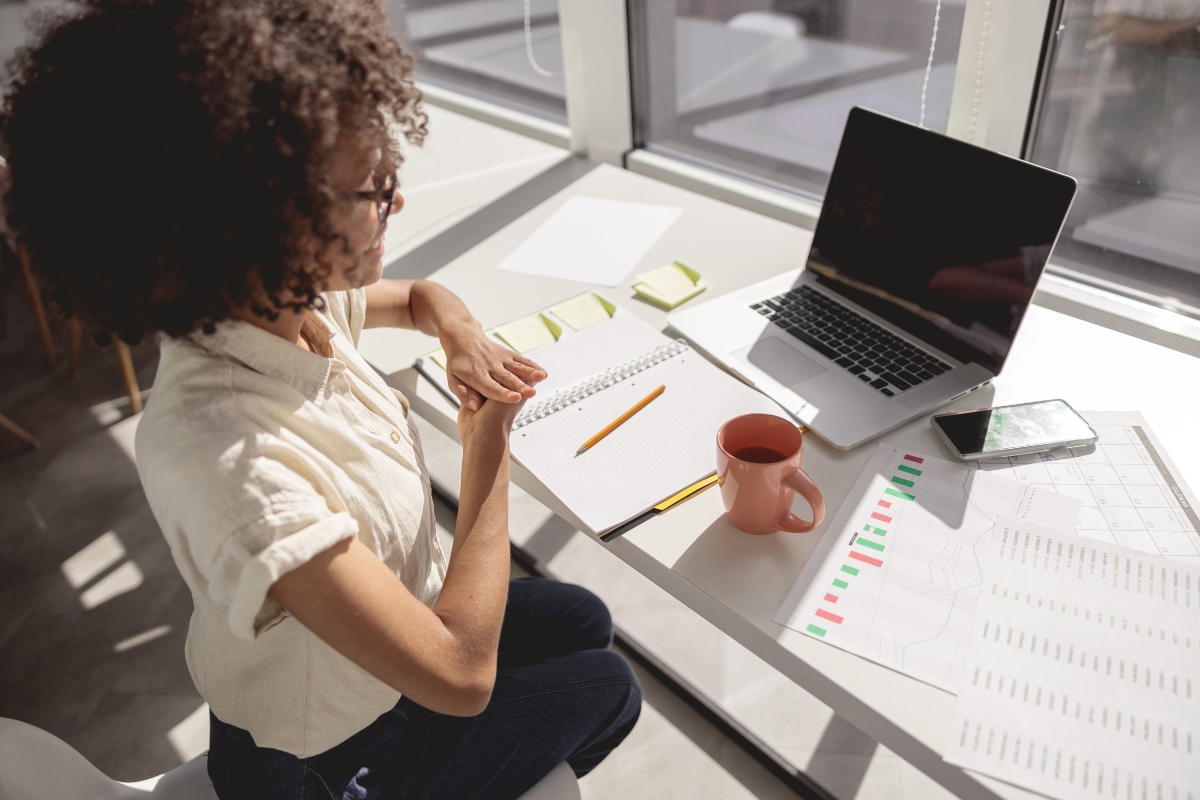 A woman seated at a desk with a laptop and papers, working on guest posting.