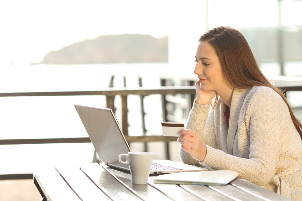 A woman sitting at a table with a laptop and credit card is ready for online shopping.