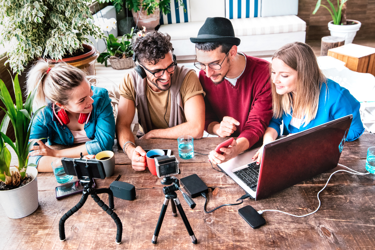 A group of digital creators sitting around a table with a laptop and a camera.