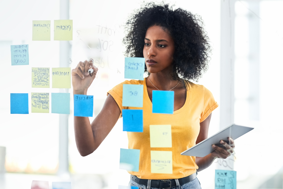 A woman holding a tablet and sticky notes on a wall, planning her content map.