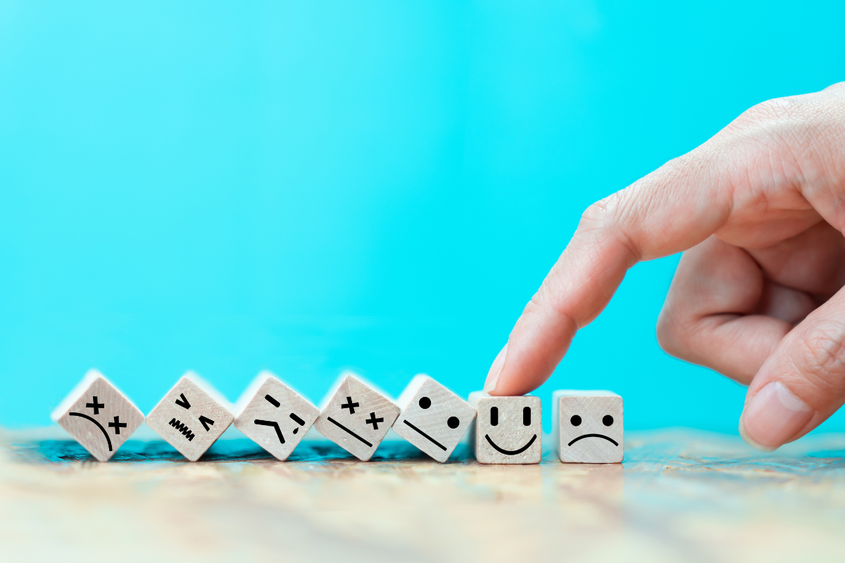 A hand is pointing to a pile of wooden blocks with smiley faces on them.