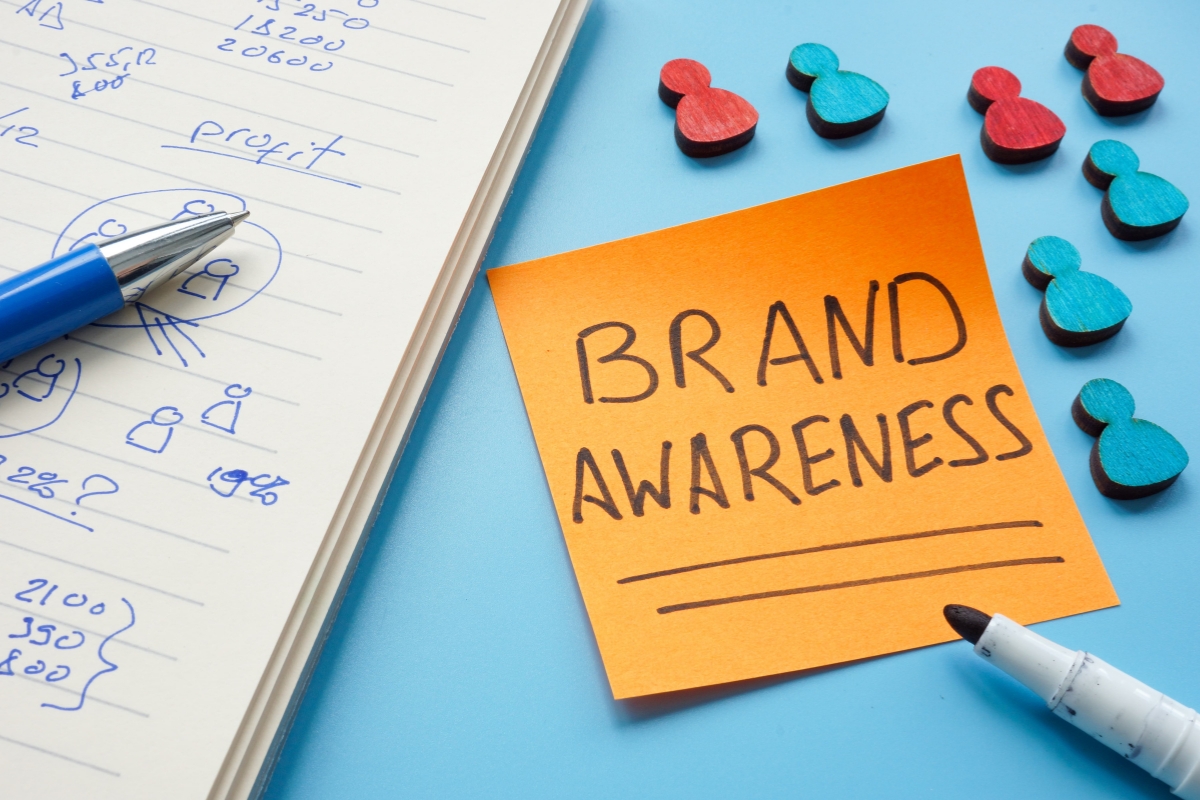 A sticky note with the words "increasing brand awareness" next to a notebook and pen.