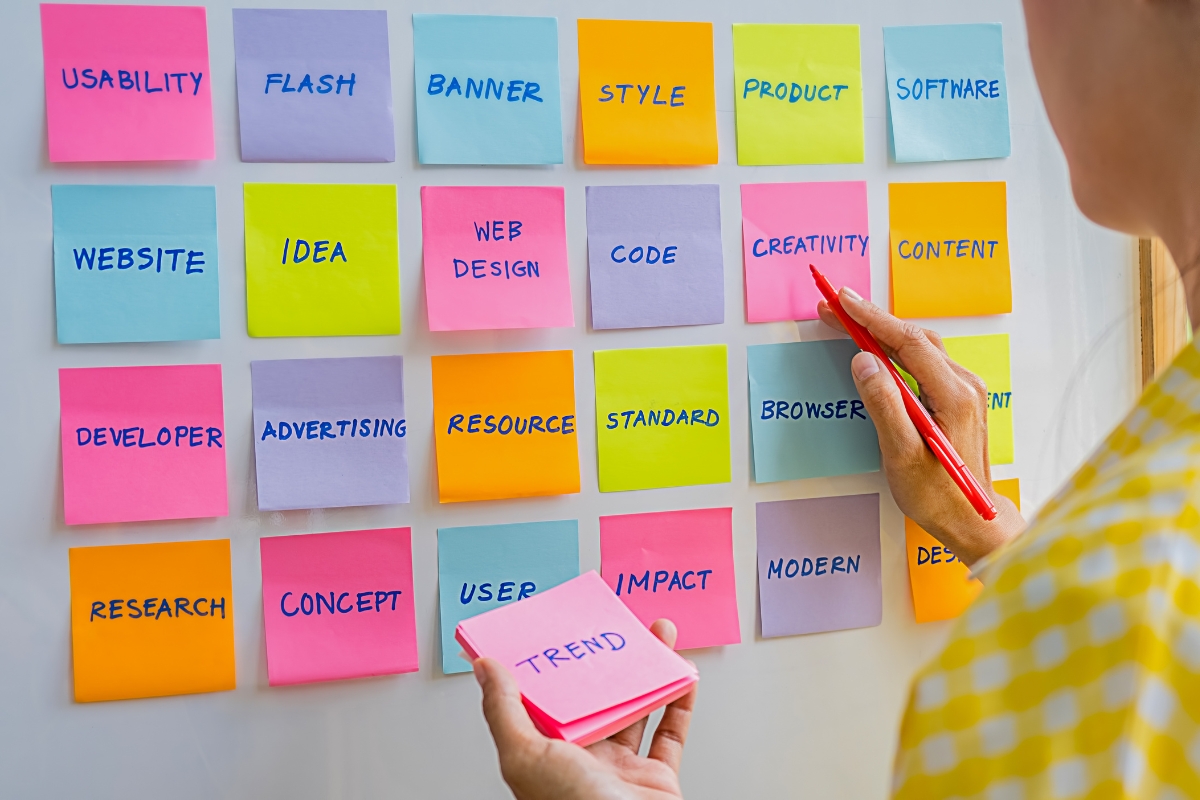 A woman is increasing brand awareness by putting sticky notes on a whiteboard.