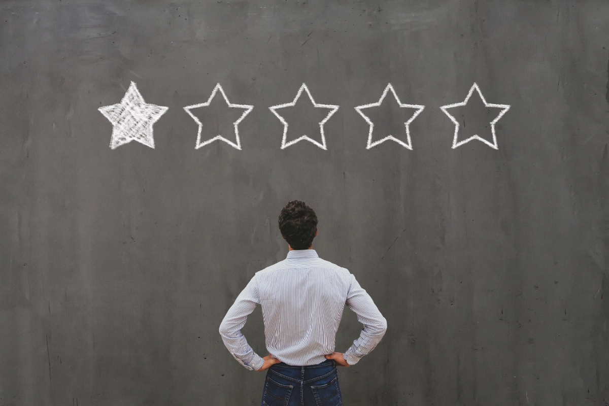 A man grimacing at a chalkboard with five stars drawn on it.