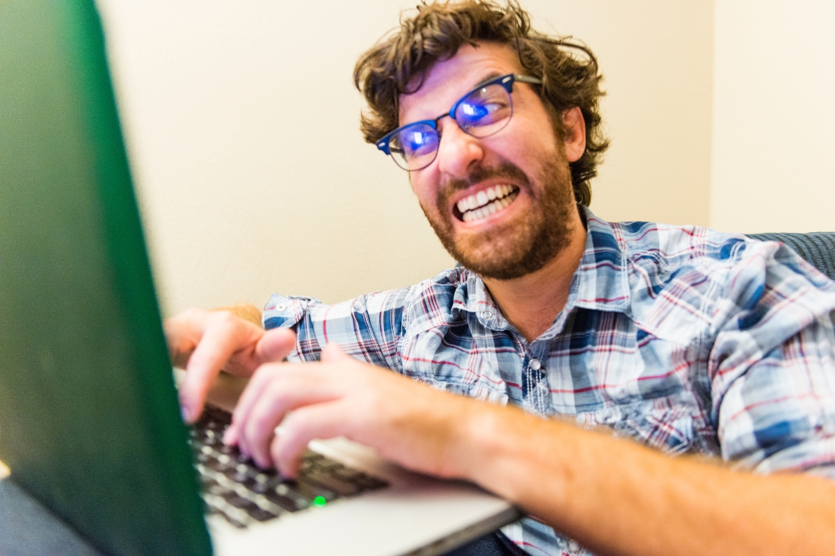 A man wearing glasses is using a laptop computer to read negative reviews.