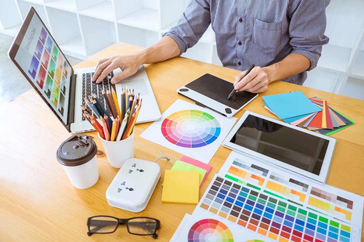 A man designing a website at a desk with a laptop and color swatches.