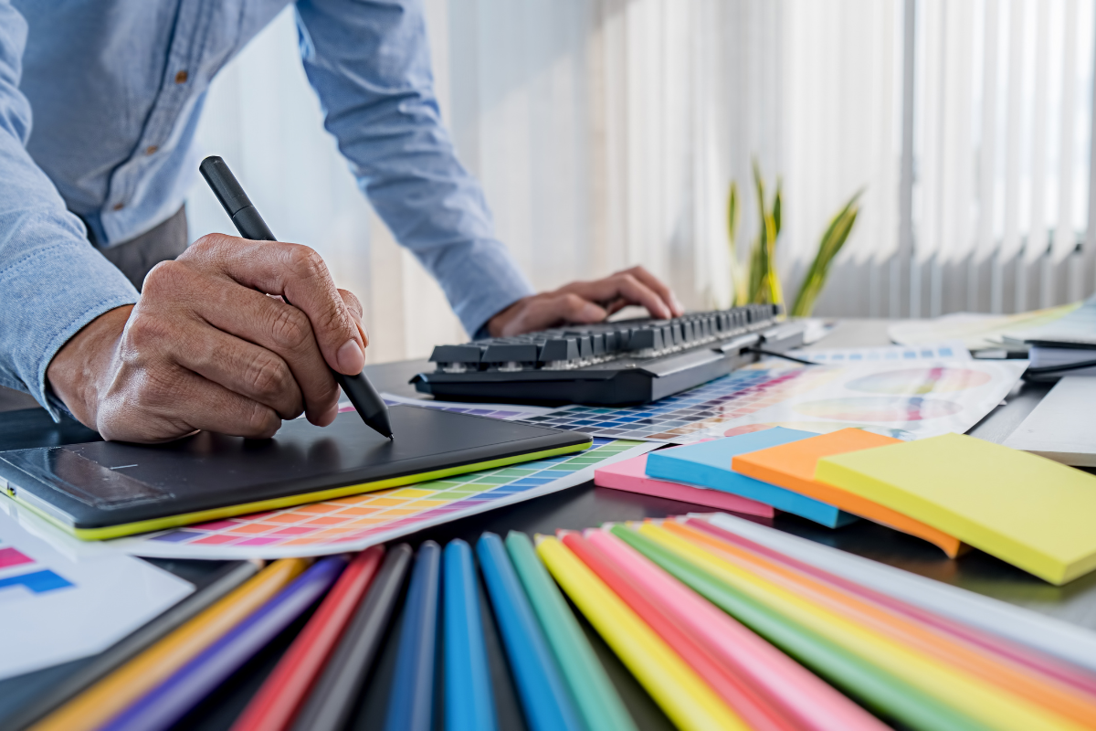 A man diligently working at a desk adorned with an array of pens and colored paper.