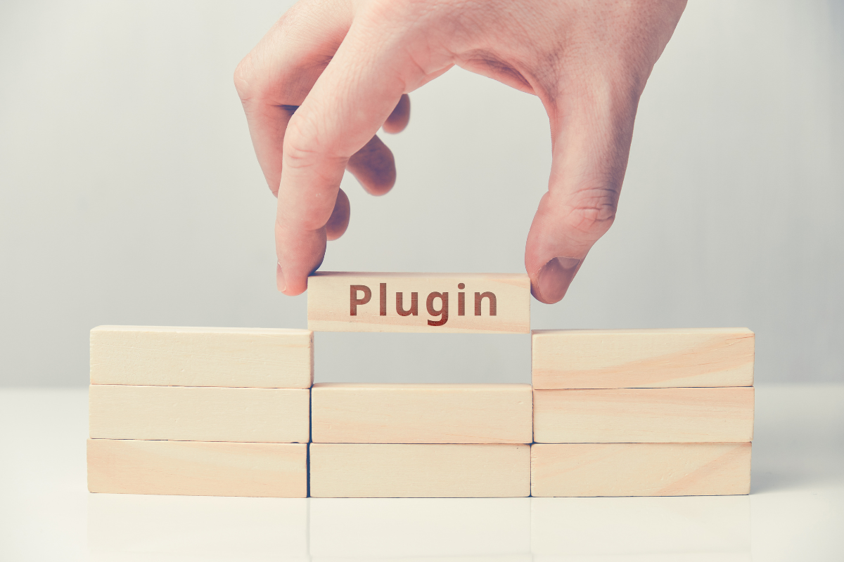 A hand holding a wooden block with the word "plugin" on it.