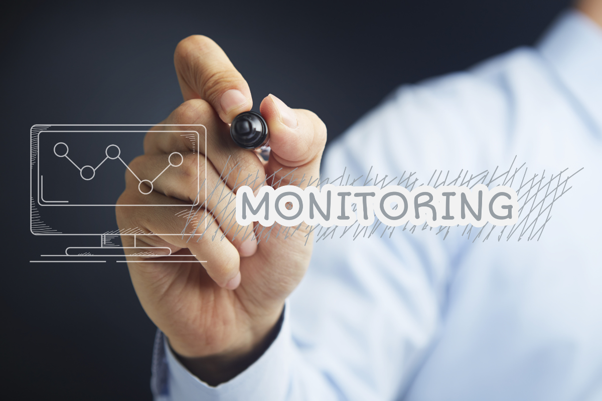 A man is writing the word "monitoring" with a computer screen.