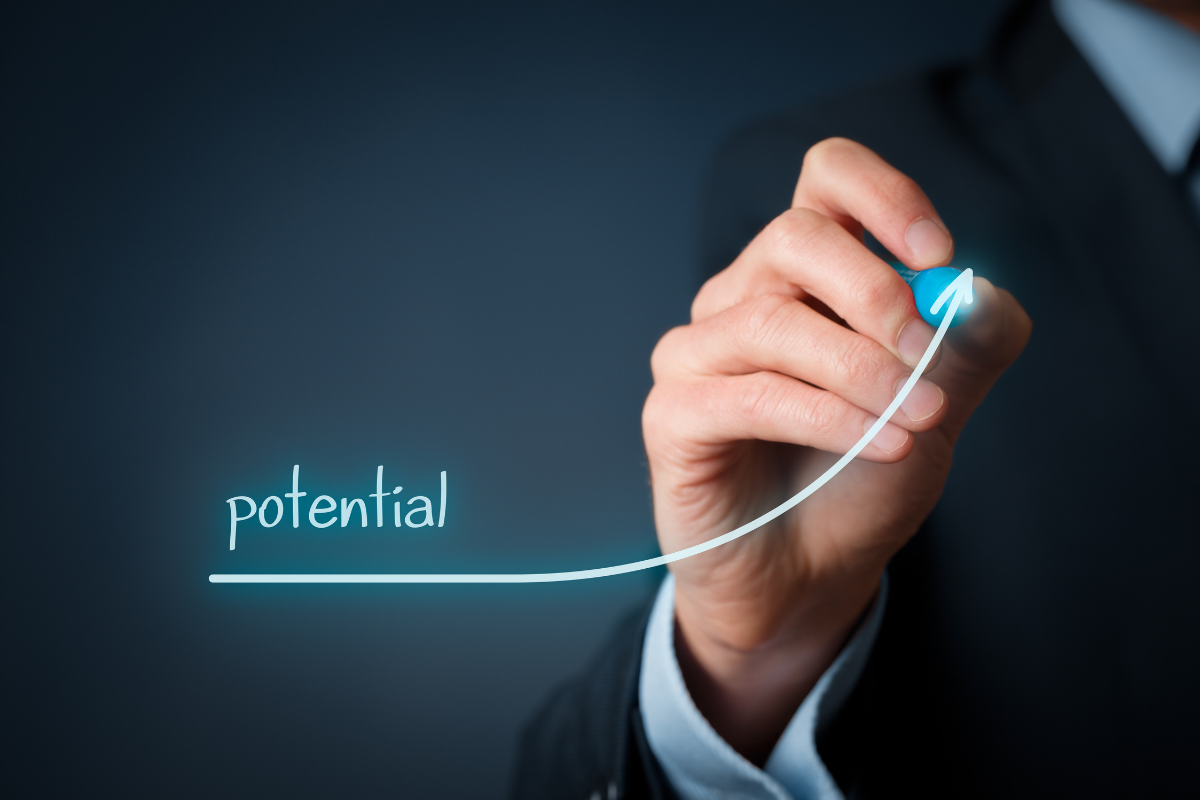 A business man writing the word "potential" with an arrow going up.