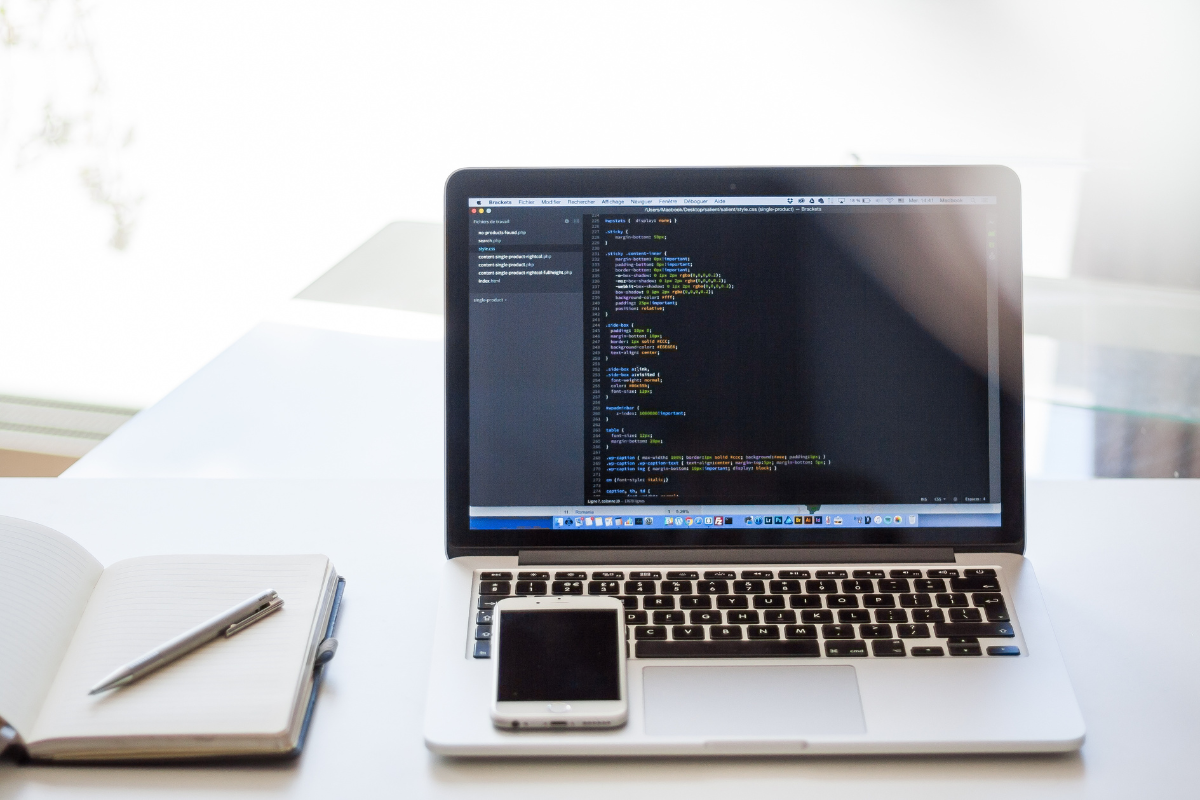 A laptop on a desk with a notebook and cell phone is common in many offices.