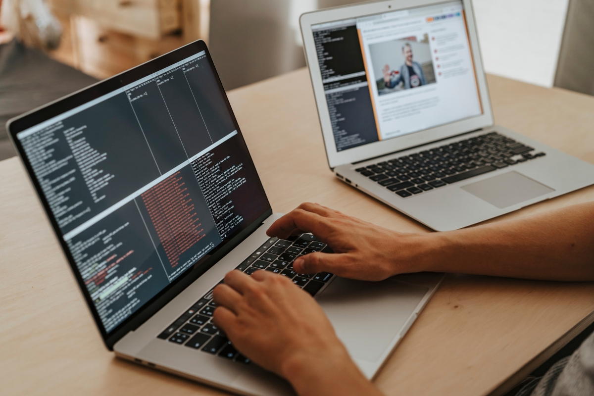 Two people working on code minification on two laptops on a wooden table.