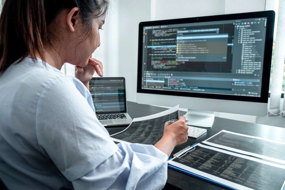 A woman sitting at a desk looking at a computer screen, focusing on code minification.