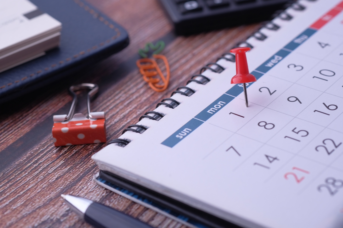 Desk with an open content calendar, a red pushpin on a Monday, a pen, and decorative paper clips.