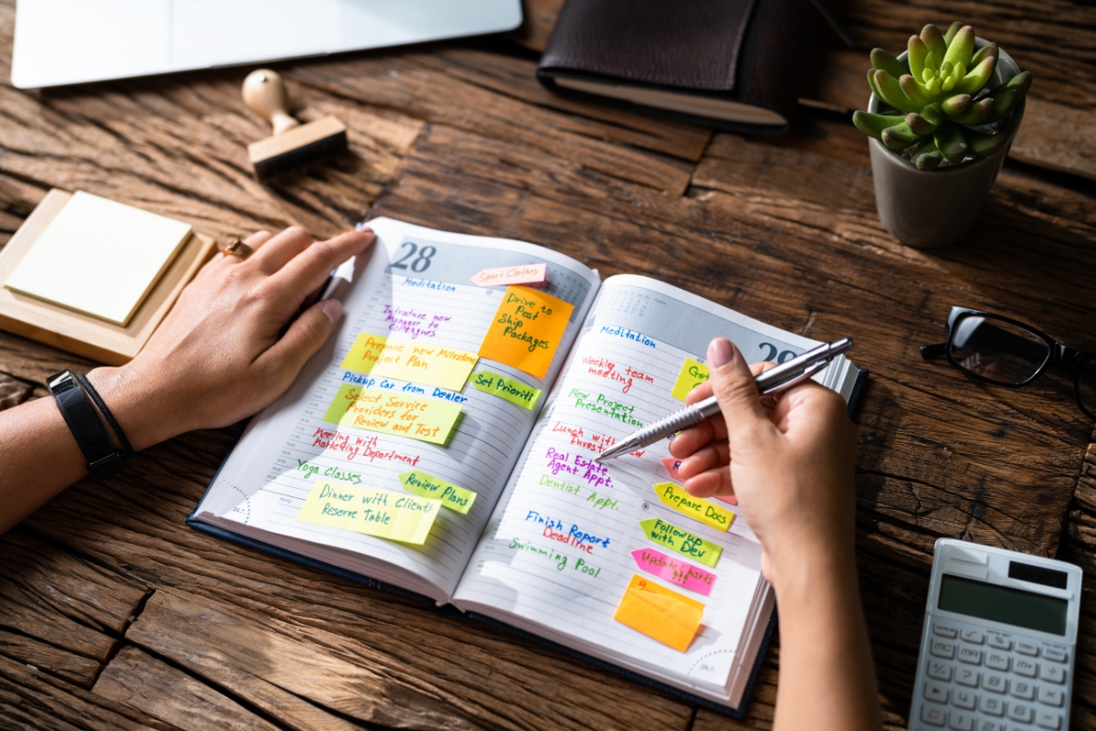 A person writing in a colorful, well-organized content calendar on a wooden desk, surrounded by office supplies.