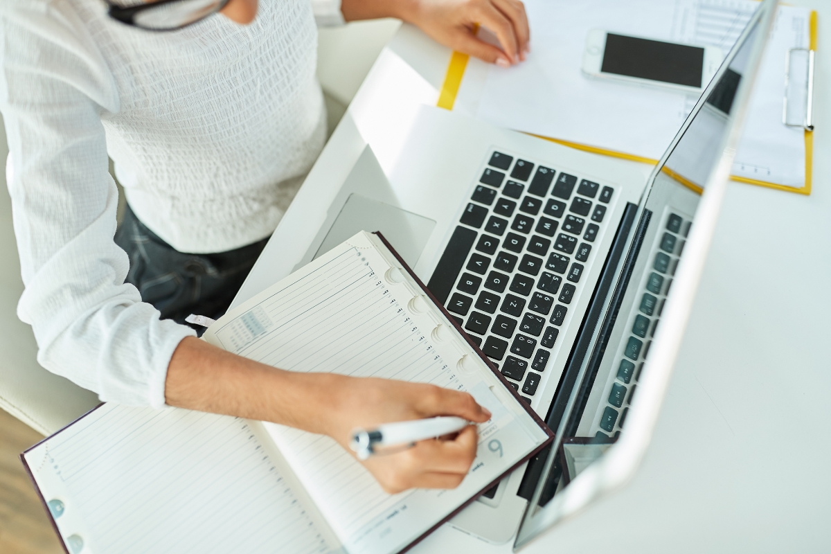 Person taking notes for a content calendar from a laptop onto a notepad.