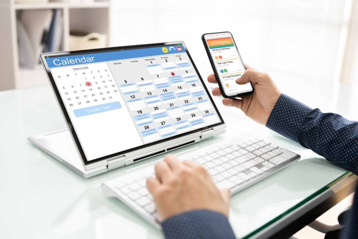 A person at a desk using a laptop with a content calendar on the screen and a smartphone displaying a to-do list application.