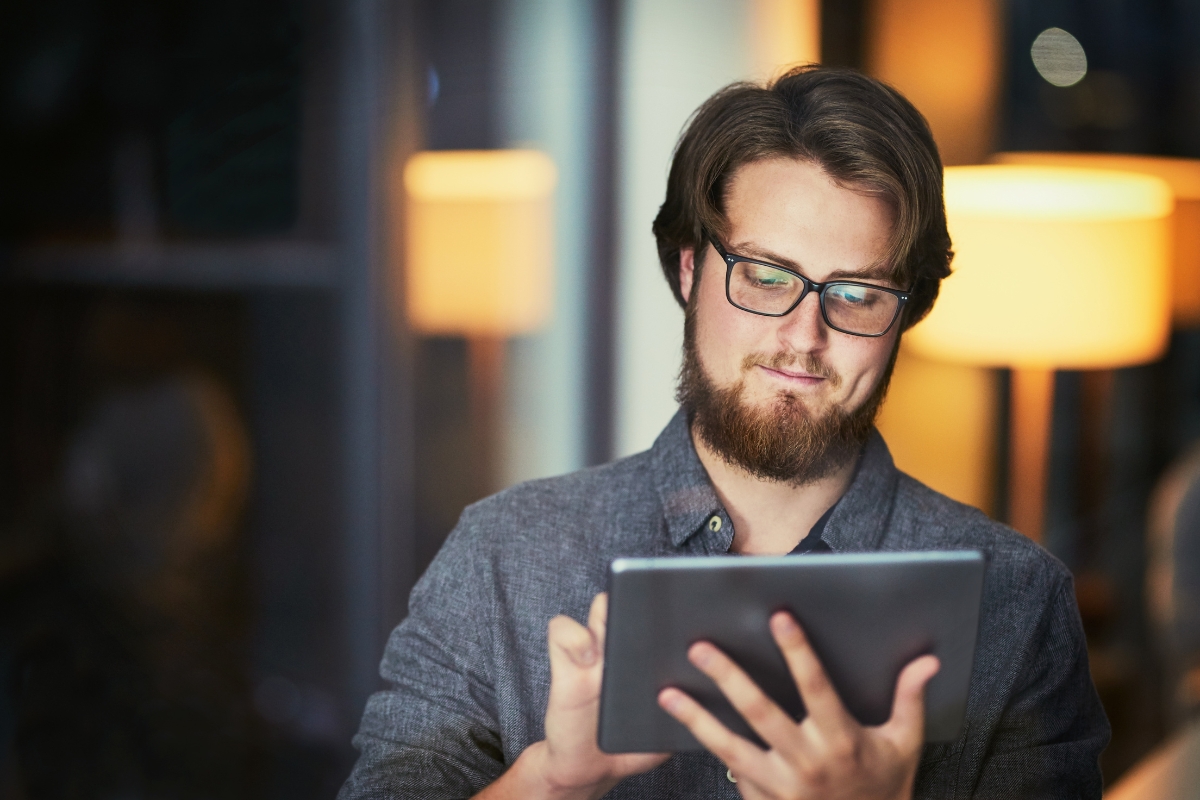 A man wearing glasses is using a tablet computer for content syndication.