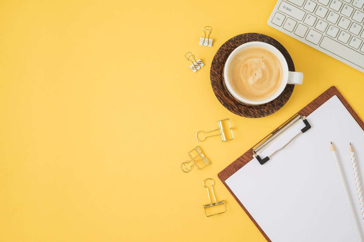 A cup of coffee and a clipboard on a yellow background, ready for content syndication planning.