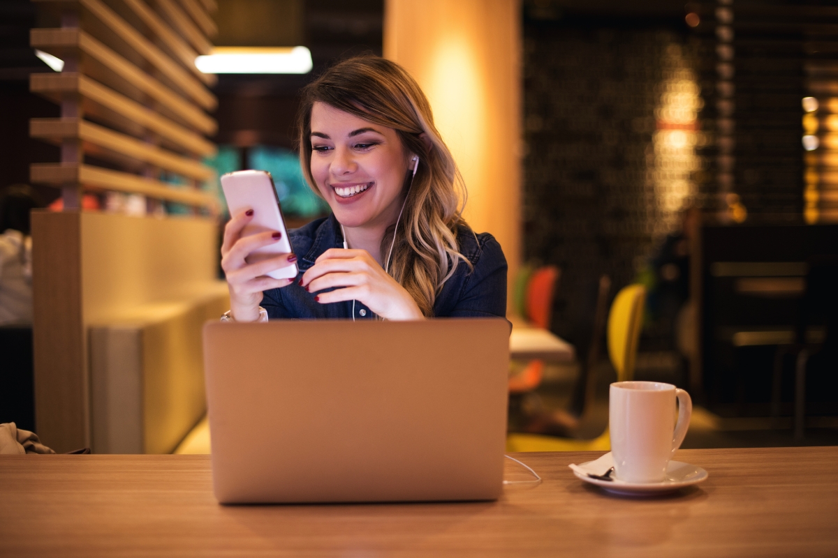 A woman sitting at a table with a laptop and cell phone, working on content syndication.