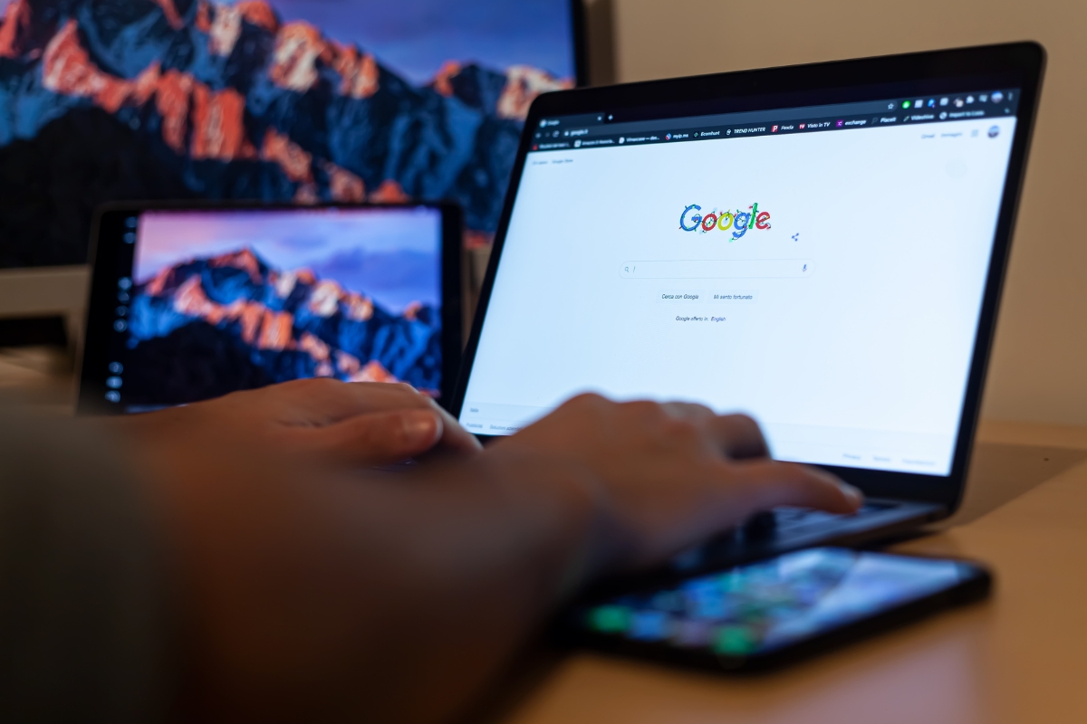 Person using a laptop with Google Guaranteed local services search homepage on the screen, with a smartphone and tablet also in view.