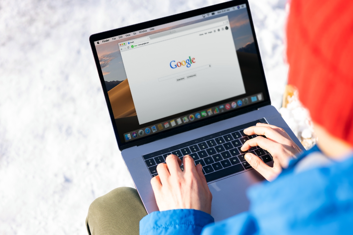 Person using a laptop with Google Guaranteed Local Services search engine on the screen, outdoors on a sunny day with snow in the background.