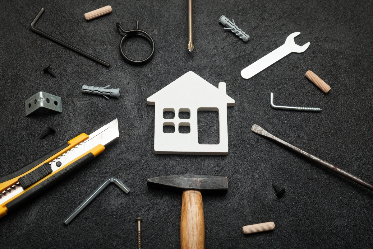 Assorted DIY tools and a house-shaped cutout from home service companies arranged on a dark surface.