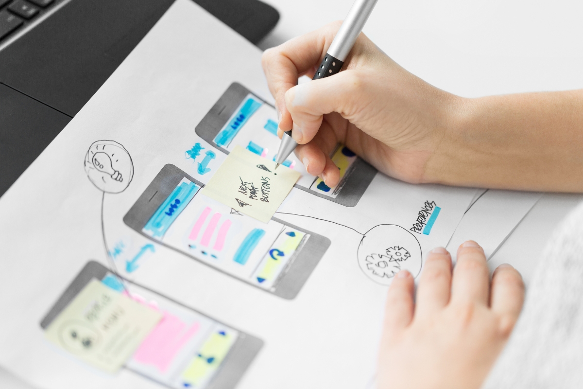 A person sketching how to create wireframes for a mobile app interface on paper with annotations and icons.