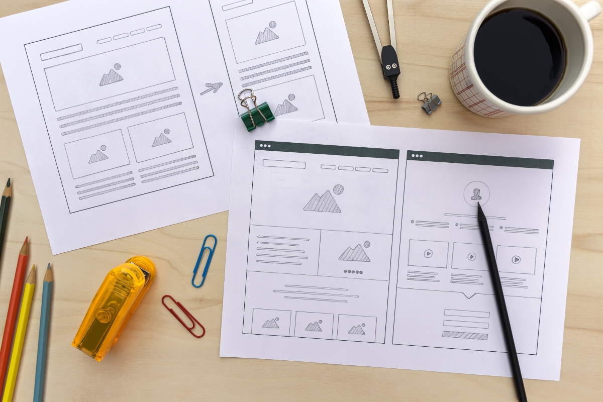 Wireframe sketches on how to create wireframes for a website layout on a desk surrounded by design tools and a cup of coffee.